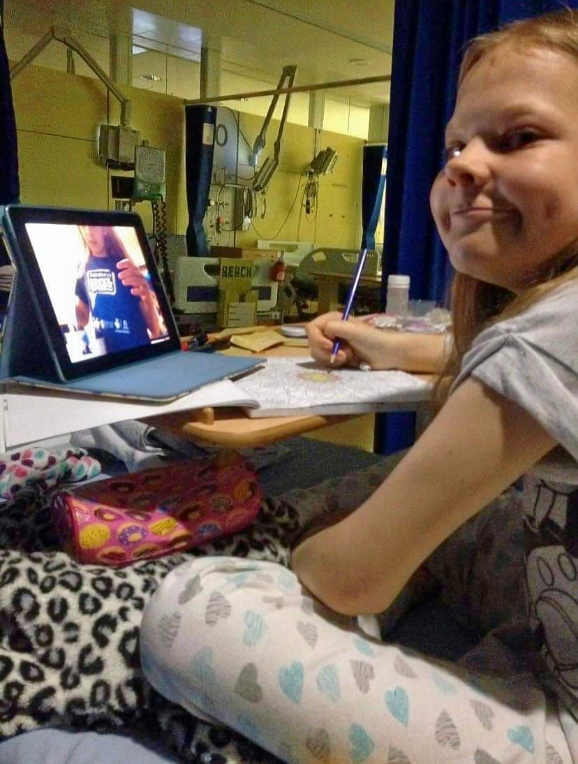 Emily in her hospital bed with her iPad and colouring book