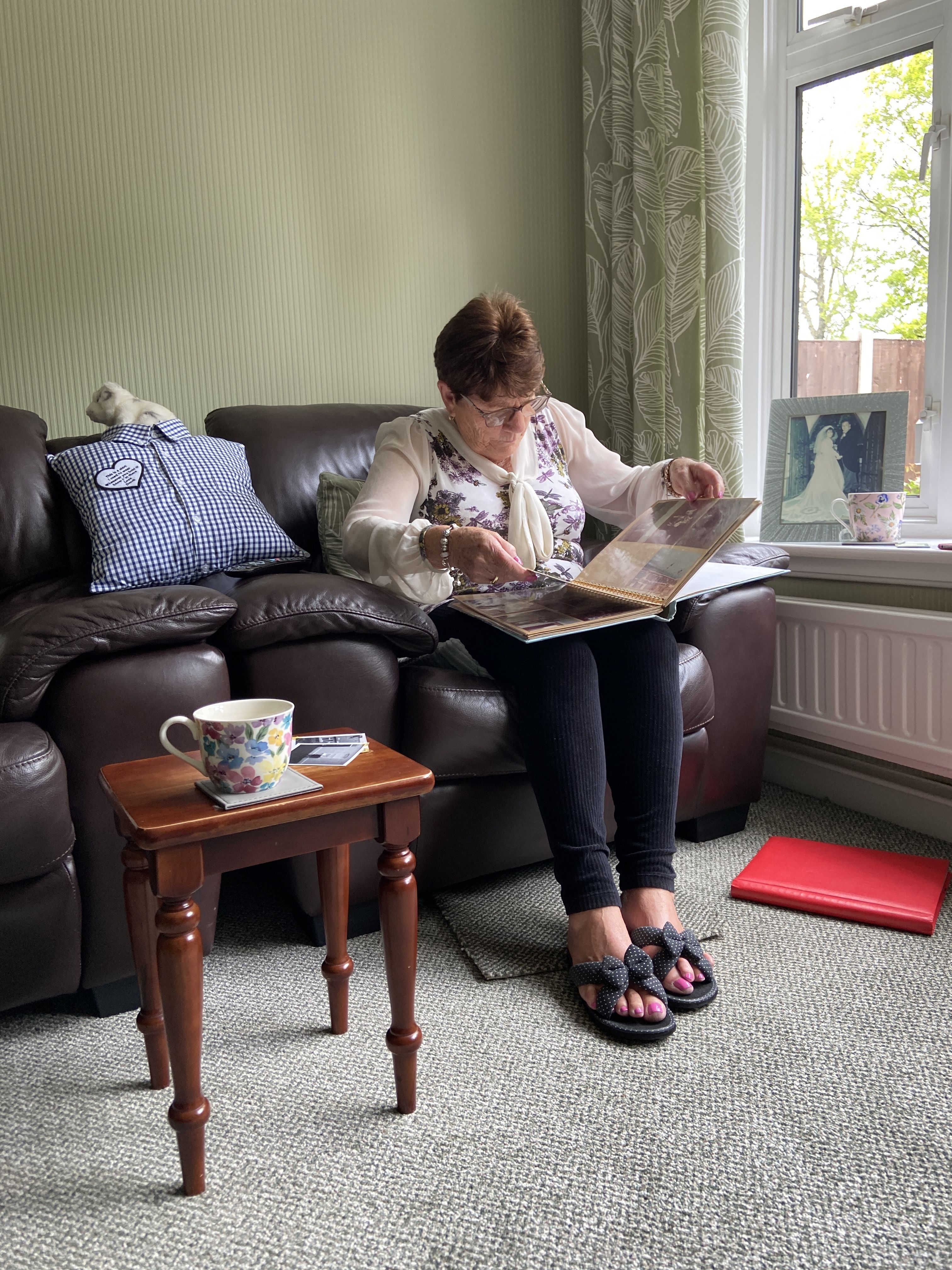 Alice sitting in a chair, looking through old photo albums with a thoughtful expression.