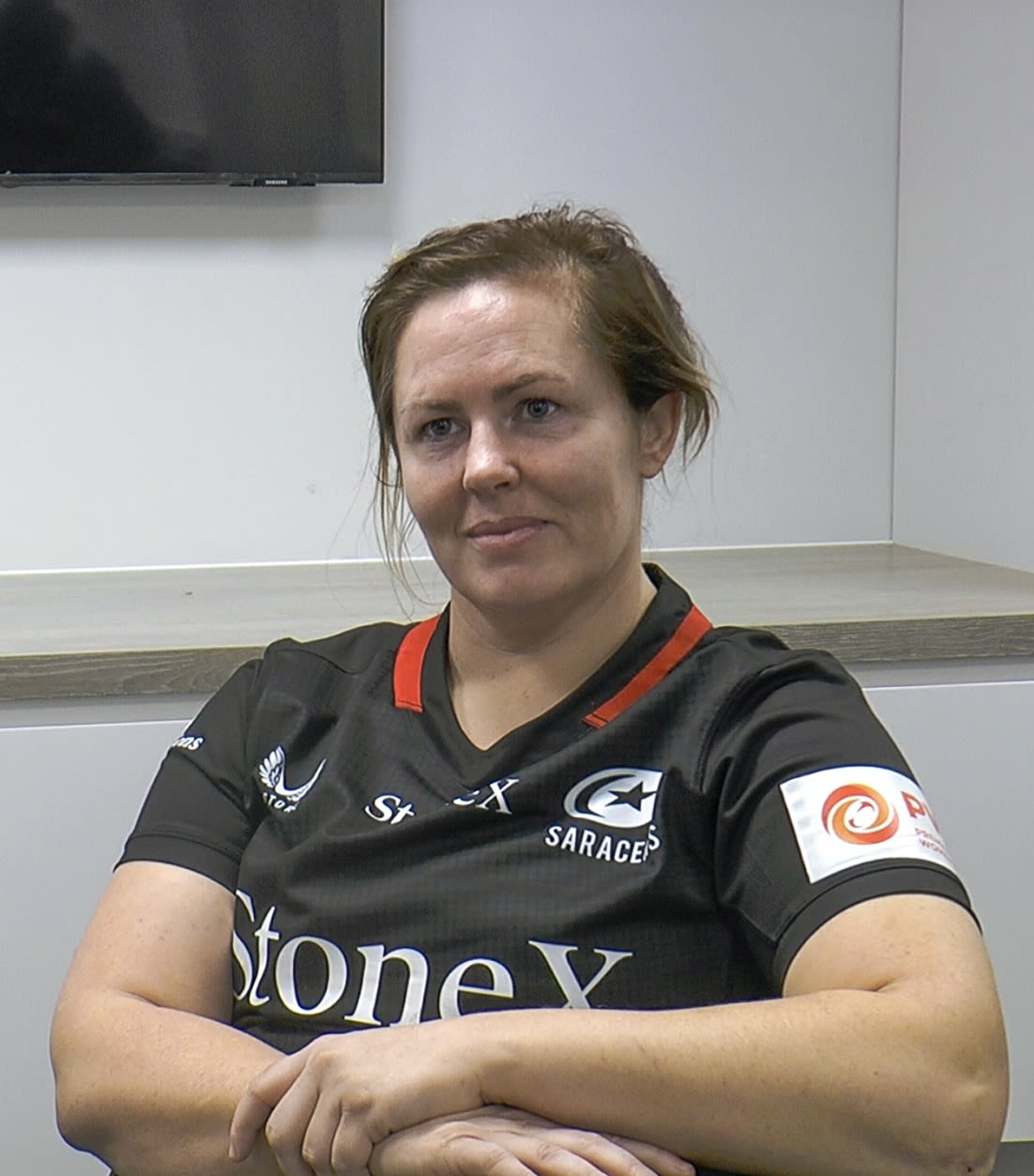 Marlie Packer in Saracens kit sitting cross-armed in the Media room at StoneX Stadium