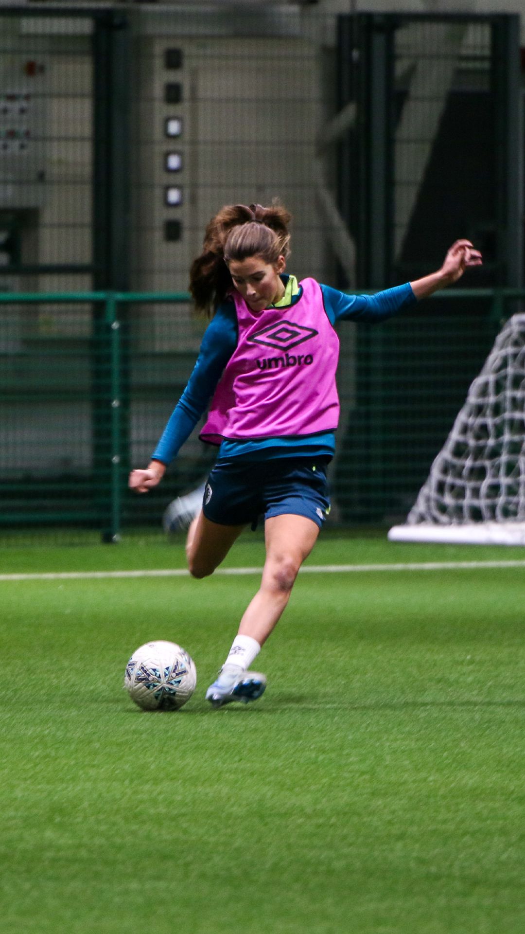 Eloise Hall about to kick a football. She is wearing AFC Bournemouth training kit and a pink umbro bib